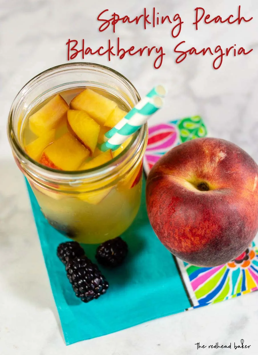 An overhead shot of a glass of sparkling blackberry peach sangria, a fresh peach and three blackberries.