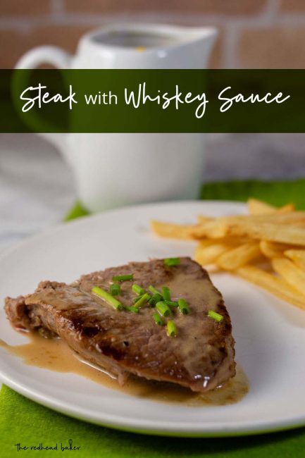 A plate of steak with whiskey sauce and a side of French fries with a container of whiskey sauce in the background