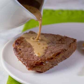 Whiskey sauce being poured onto a piece of sirloin steak