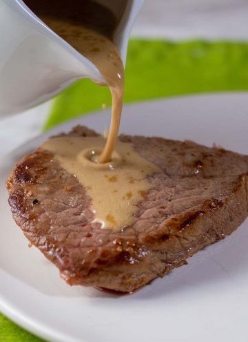 Whiskey sauce being poured onto a piece of sirloin steak