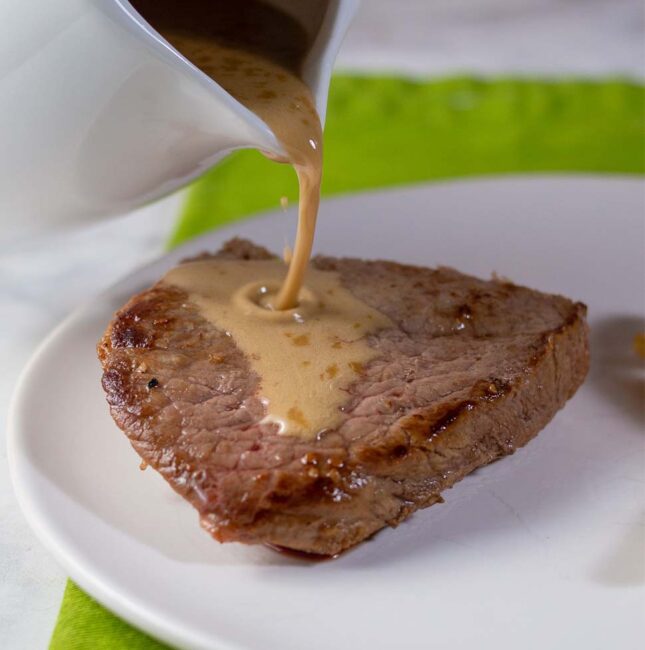 Whiskey sauce being poured onto a piece of sirloin steak