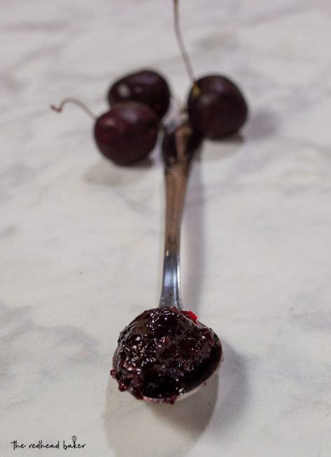 A spoonful of cherry amaretto preserves with cherries in the background.