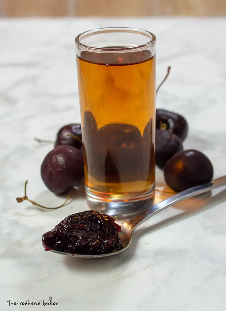 A spoonful of cherry amaretto preserves with a shot glass of amaretto and fresh sweet cherries.