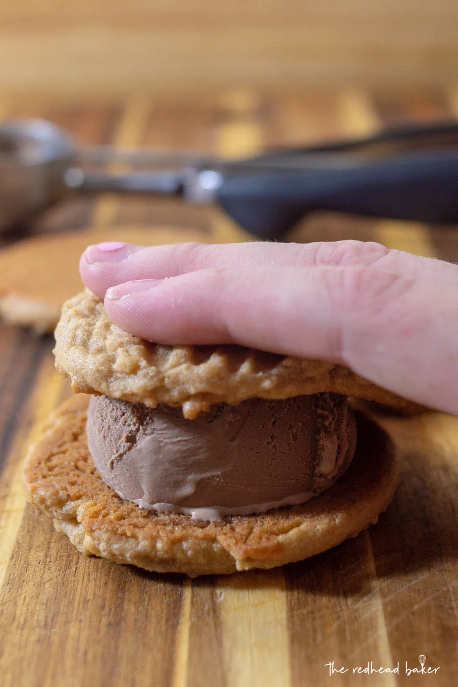 A hand pressing down on a chocolate peanut butter ice cream sandwich