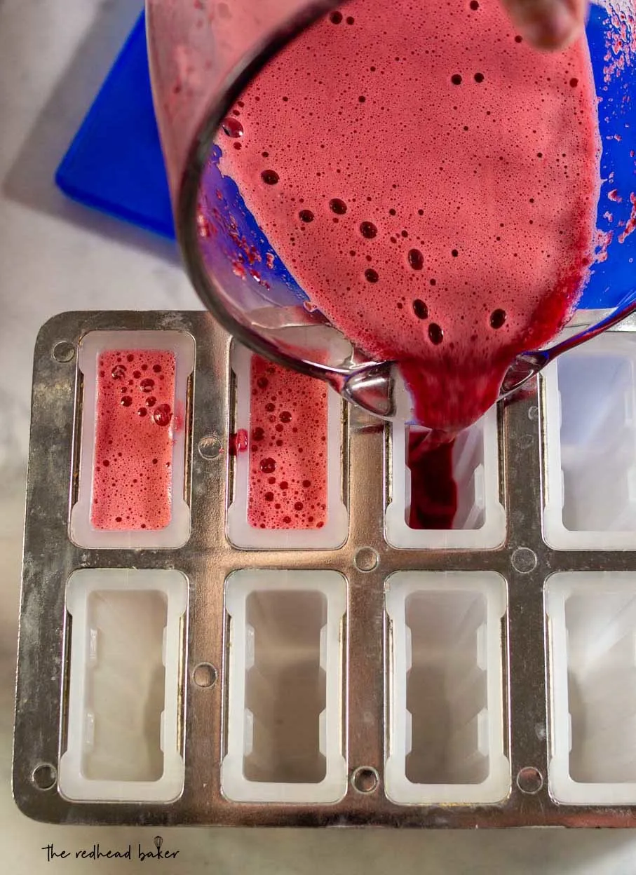 Cherry limeade mixture being poured into a popsicle mold.