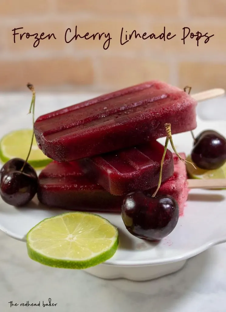 Three cherry limeade pops stacked on top of each other on a mini dessert stand with lime slices and cherries.