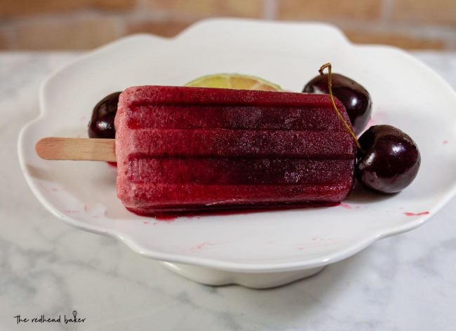 One cherry limeade pop on a mini dessert stand with a few cherries.