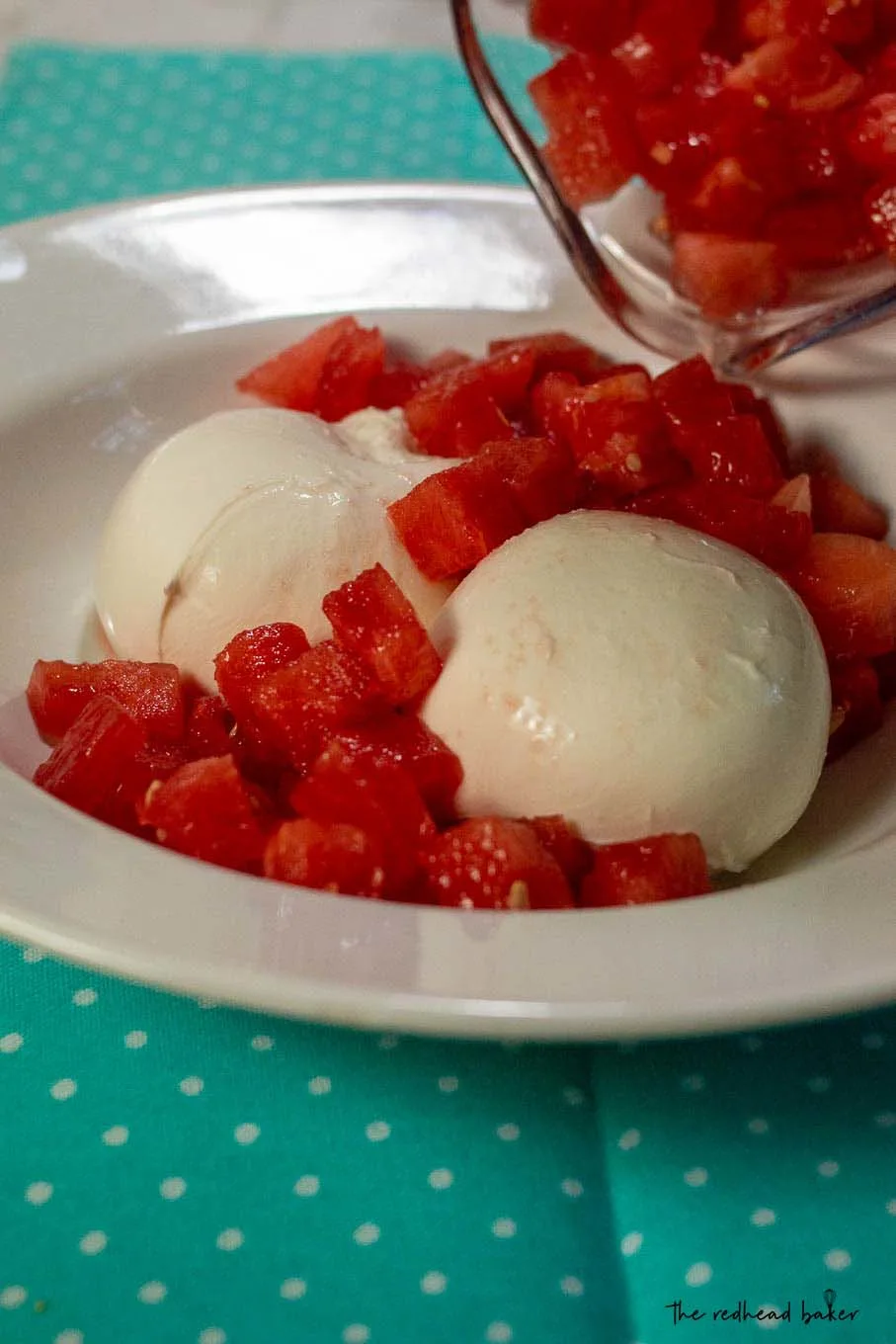 Watermelon being poured into a dish with two balls of burrata