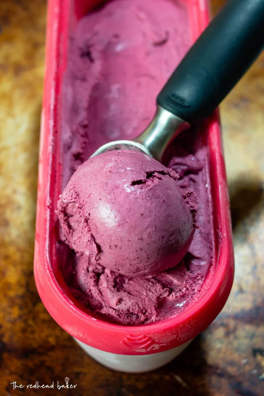 An ice cream scooper in a container of bourbon roasted cherry ice cream