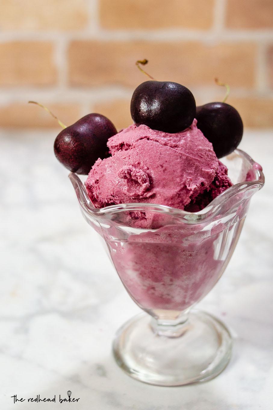 A dish of bourbon roasted cherry ice cream with three fresh cherries on top