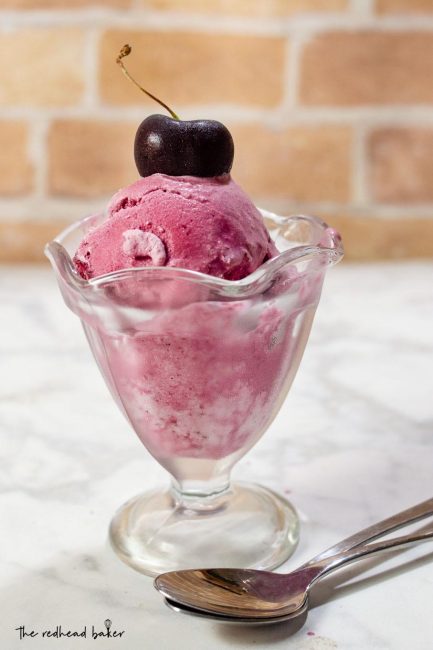 A dish of bourbon roasted cherry ice cream with a fresh cherry on top