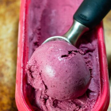 An ice cream scoop in a container of bourbon roasted cherry ice cream