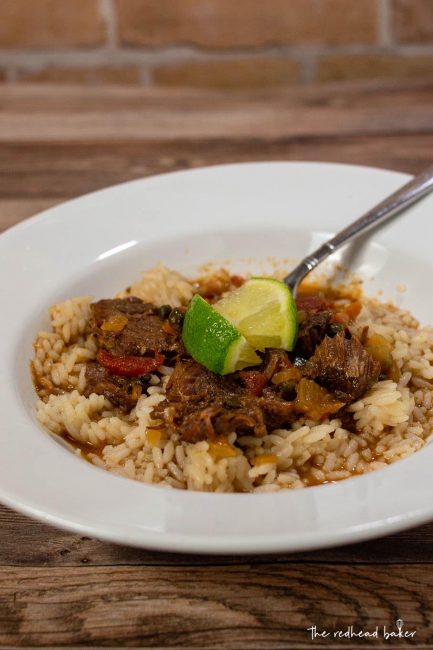 A dish of Cuban Ropa Vieja with lime wedges for garnish