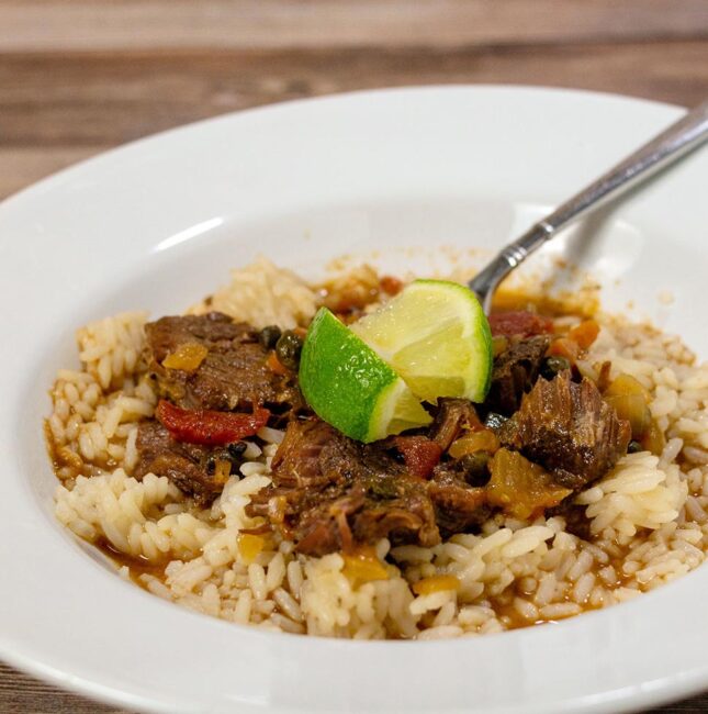 A dish of ropa vieja over rice with lime wedge garnishes