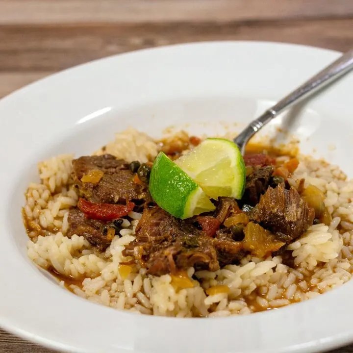 A dish of ropa vieja over rice with lime wedge garnishes