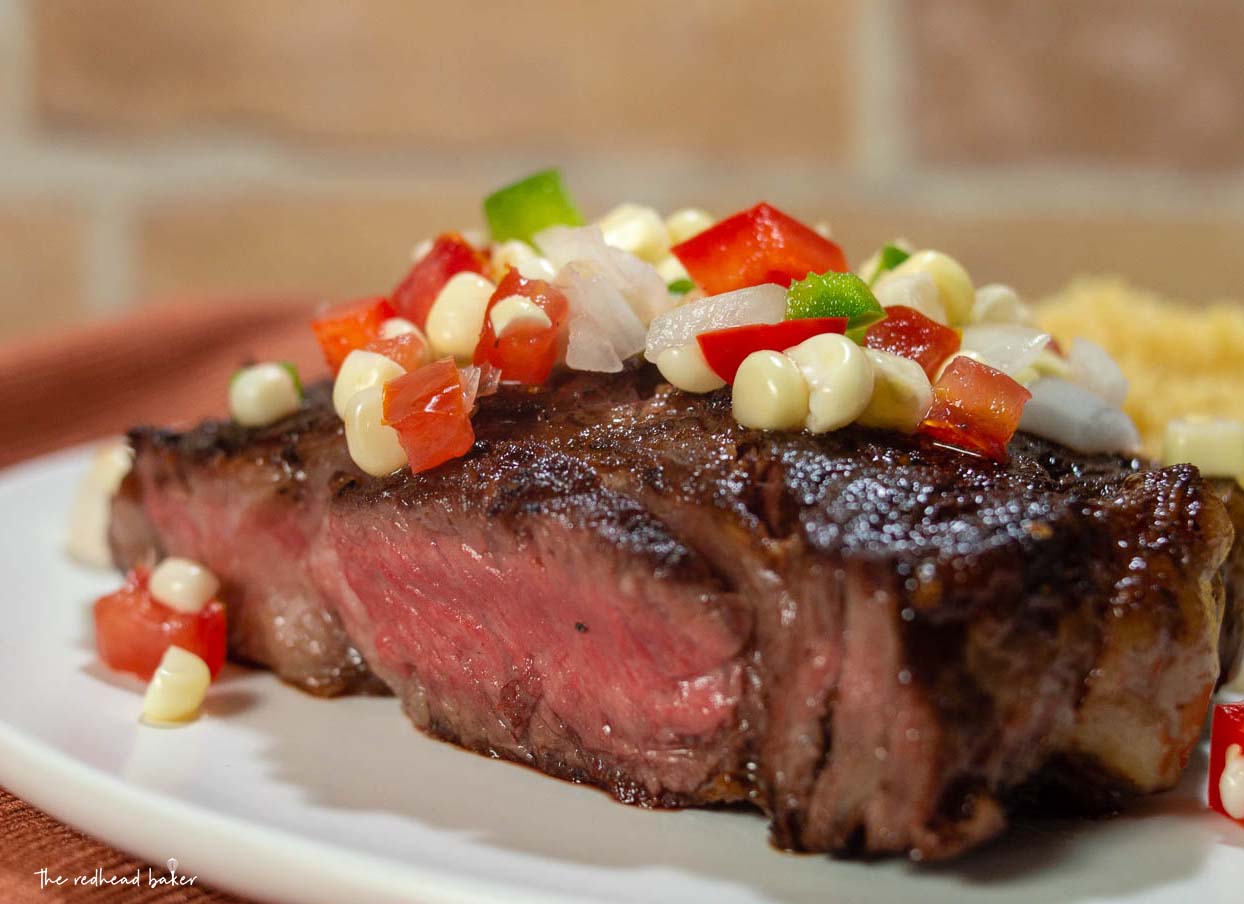 A close-up shot of a ribeye steak topped with corn salsa.