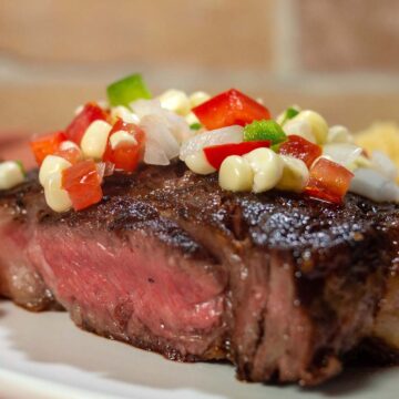 A close-up shot of a ribeye steak topped with corn salsa.