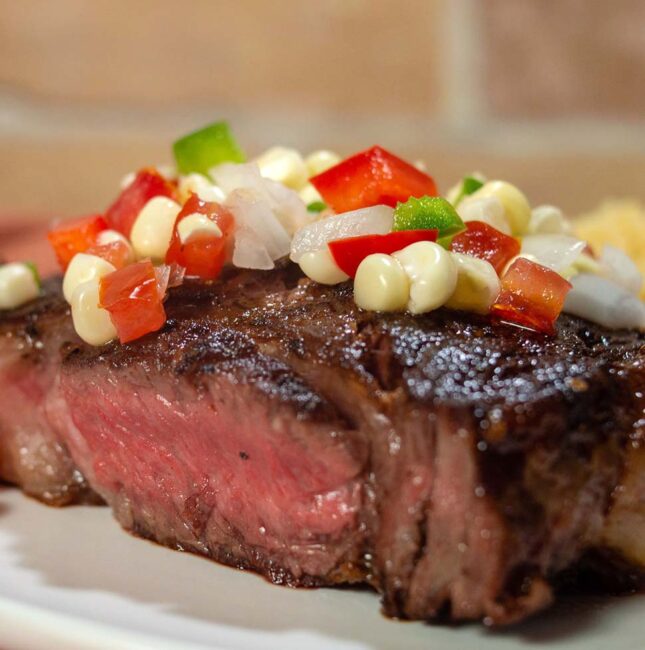 A close-up shot of a ribeye steak topped with corn salsa.