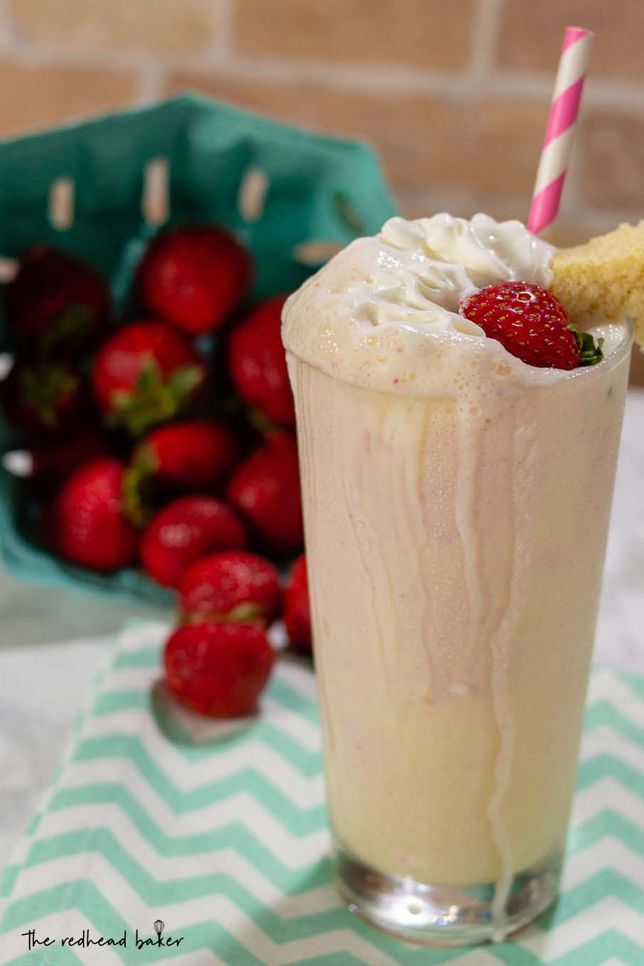 A strawberry shortcake milkshake in front of a tipped carton of fresh strawberries