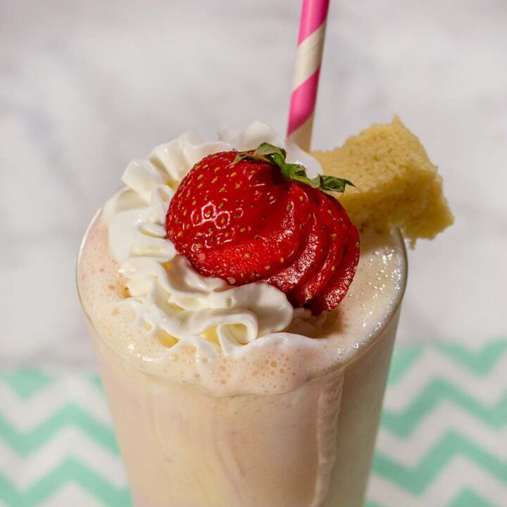 A strawberry shortcake milkshake garnished with whipped cream, a strawberry and a cube of pound cake