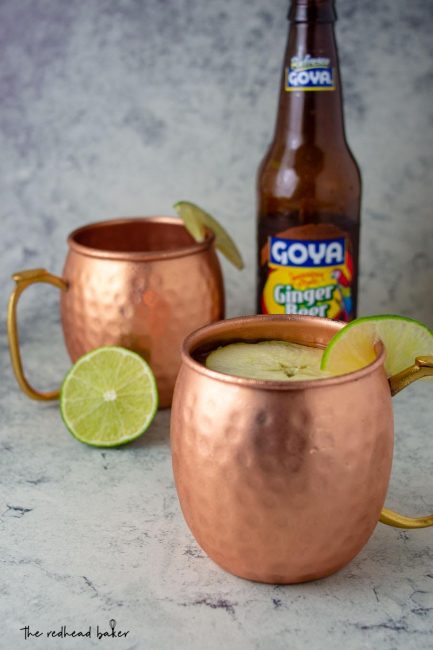 Two mugs of Apple Cider Moscow Mules in front of a bottle of ginger beer