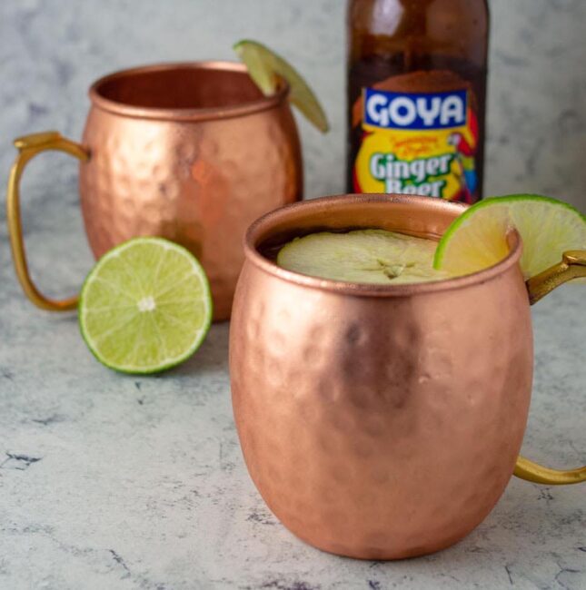 Two mugs of Apple Cider Moscow Mule in front of a bottle of ginger beer