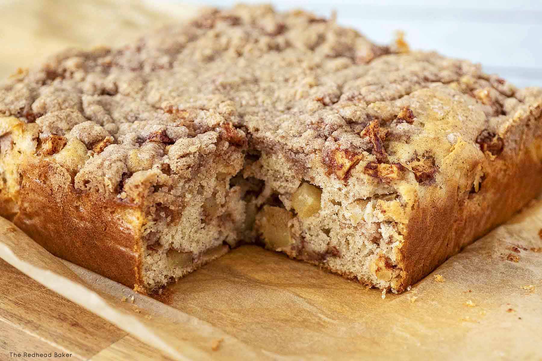 An apple crumb cake on a wooden board with a slice removed.