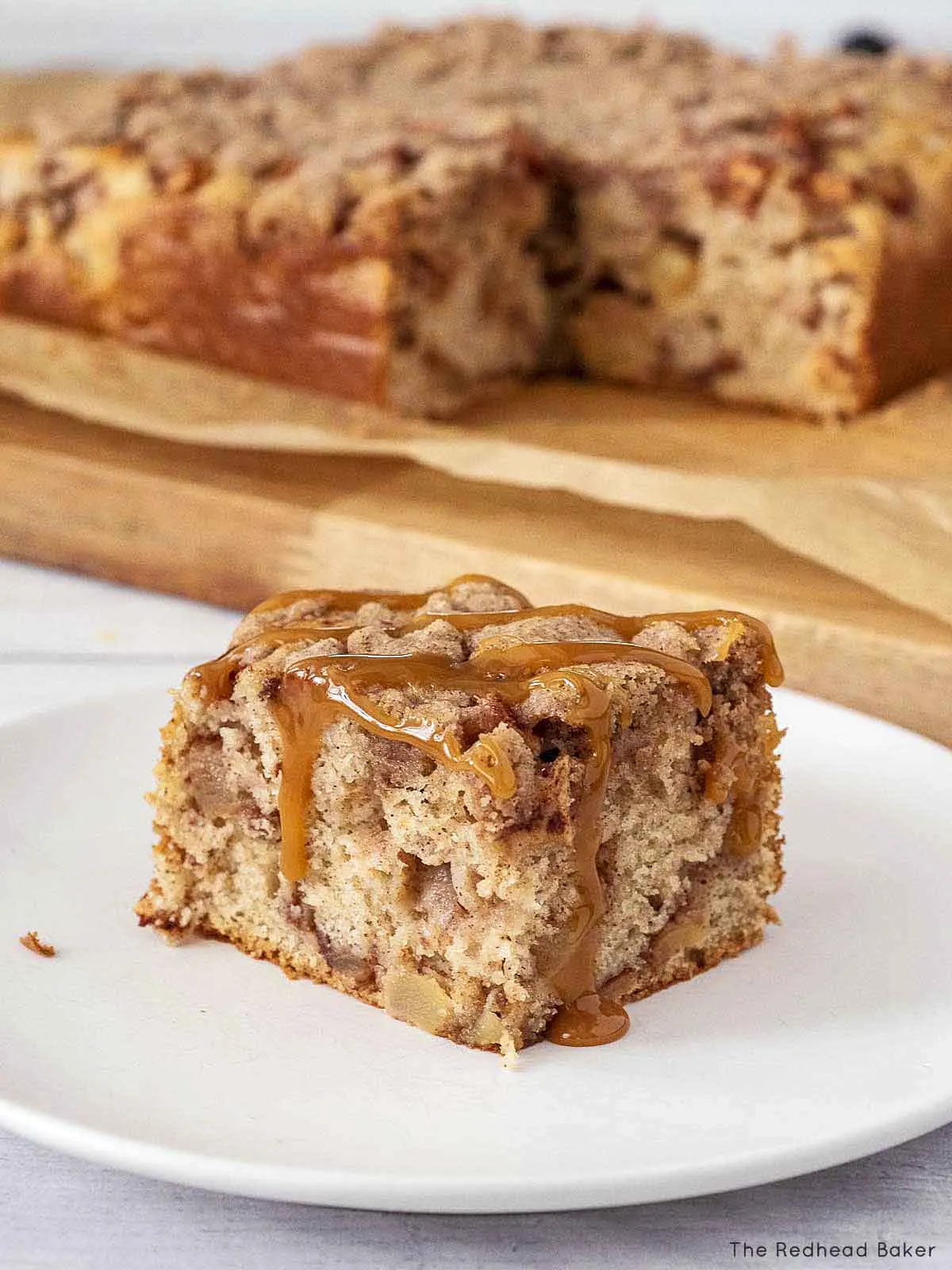 A slice of apple crumb cake topped with caramel on a white plate.