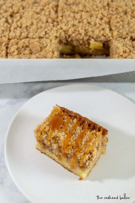A slice of caramel apple crumb cake in front of a cake pan of crumb cake