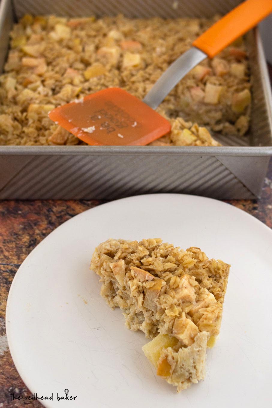 A triangle of baked apple oatmeal in front of the pan it was baked in