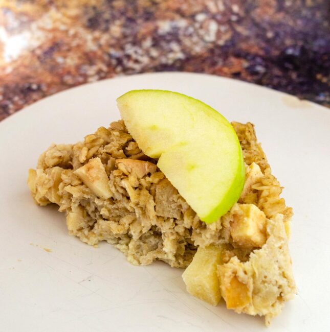 A triangle of baked apple oatmeal with a fresh apple wedge on top