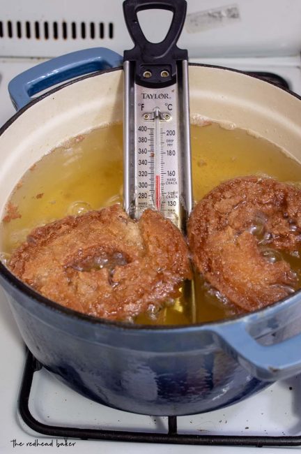 Two cider doughnuts being fried in oil.
