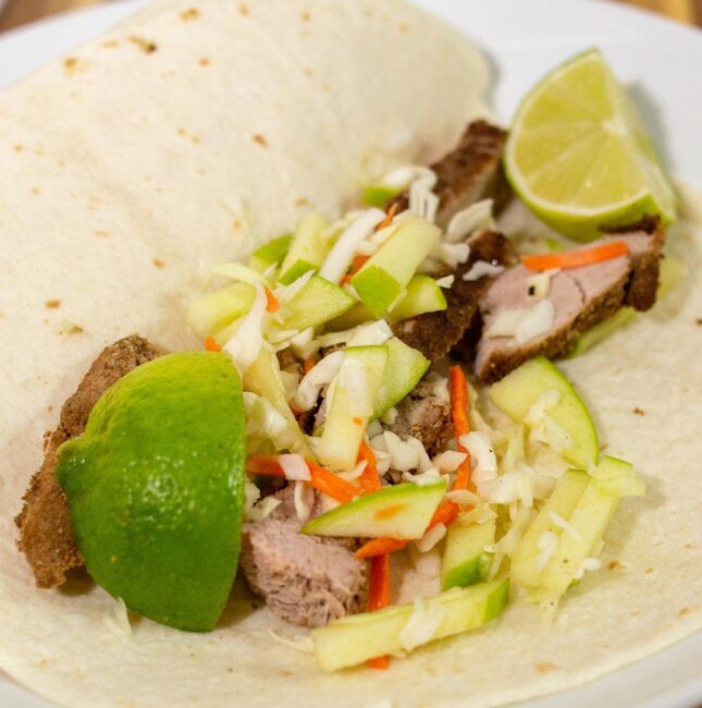 Pork tacos with apple slaw on a plate with lime wedges