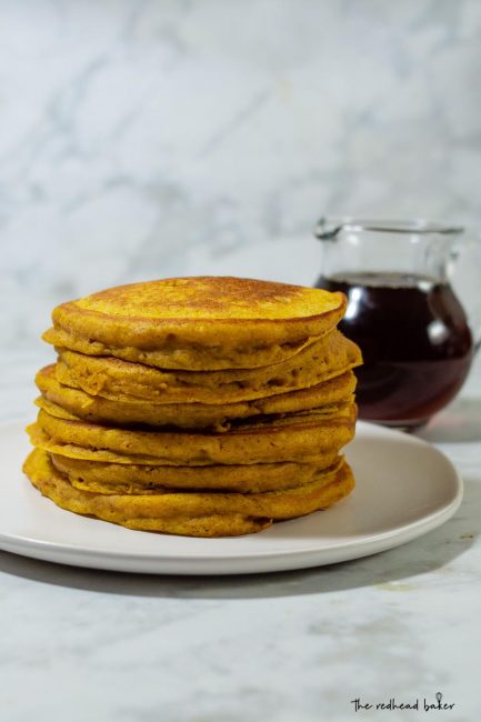 A stack of pumpkin buttermilk pancakes in front of a jar of maple syrup