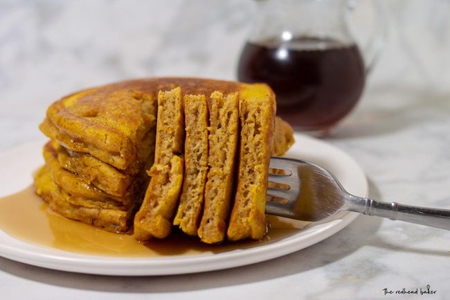 A fork holding four slices out of a stack of pumpkin buttermilk pancakes