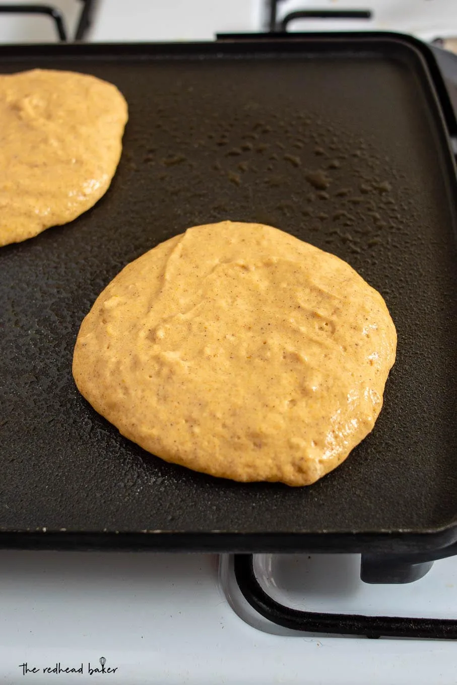 Two fluffy pumpkin buttermilk pancakes being cooked on an electric griddle
