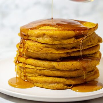 Maple syrup being poured onto a stack of pumpkin buttermilk pancakes
