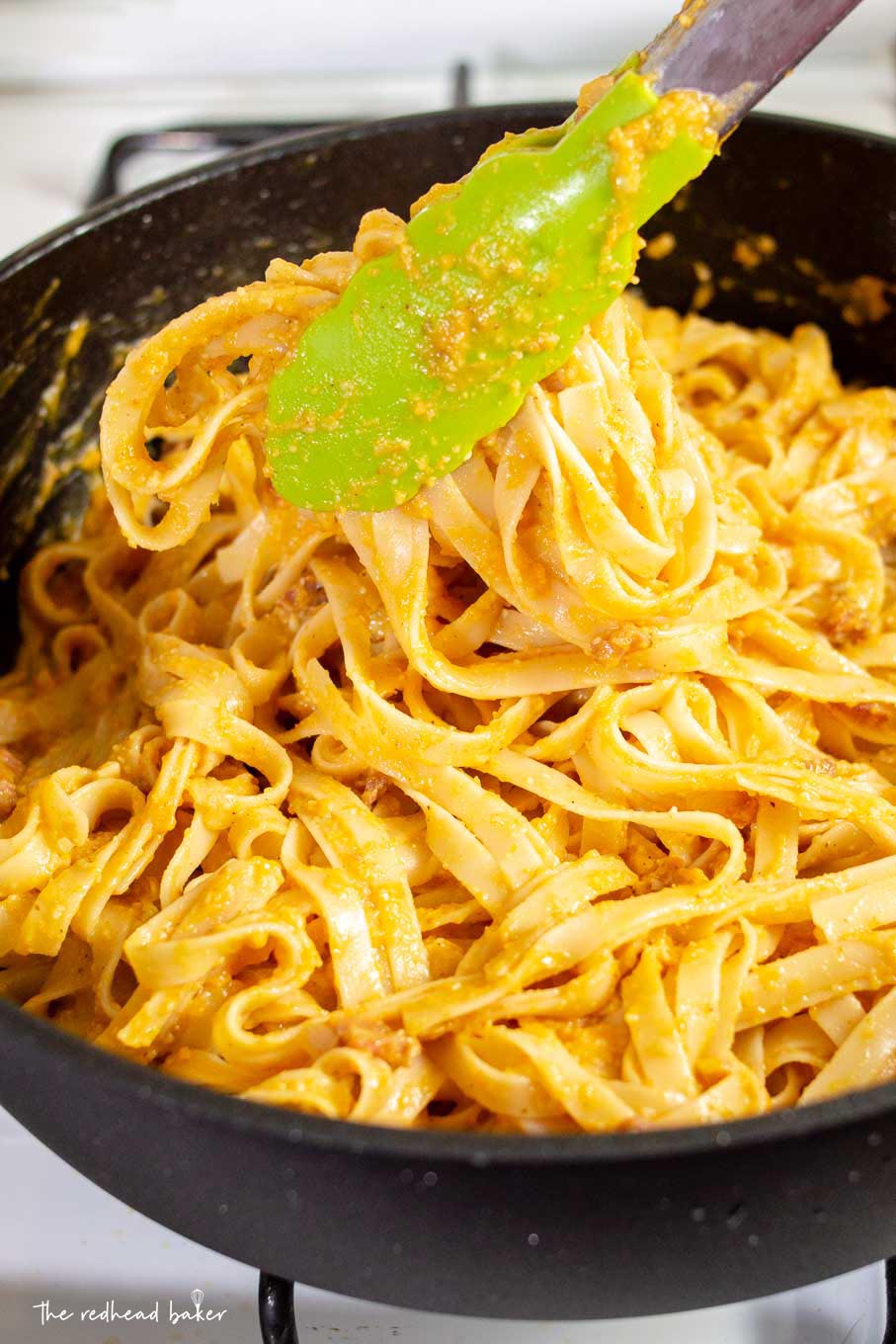 A pair of green tongs lifting up pumpkin carbonara in the saute pan.