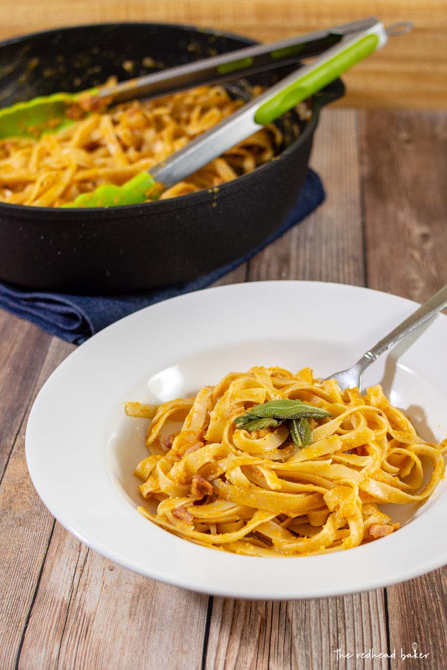 A serving of pumpkin carbonara in a serving dish in front of a saute pan of carbonara.