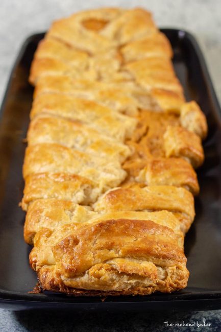 An un-iced, un-cut pumpkin cheesecake danish braid on a black serving tray.