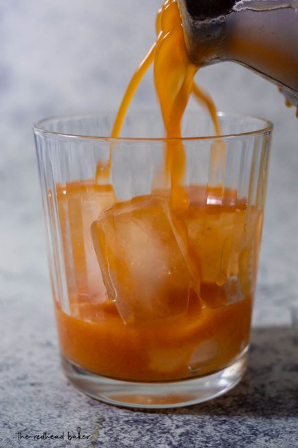 Pumpkin old-fashioned being strained into a glass filled with ice.