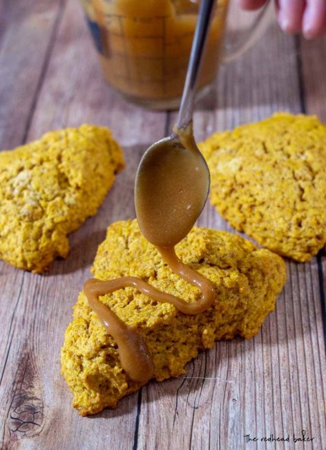 A spoon drizzling caramel glaze onto three spiced pumpkin scones.