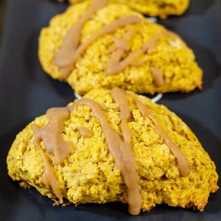 Two caramel-glazed spiced pumpkin scones on a black tray.