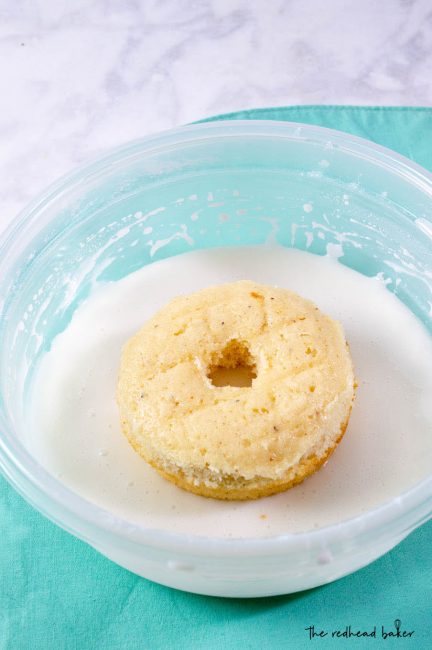 A baked lemon donut upside down in a dish of coconut glaze