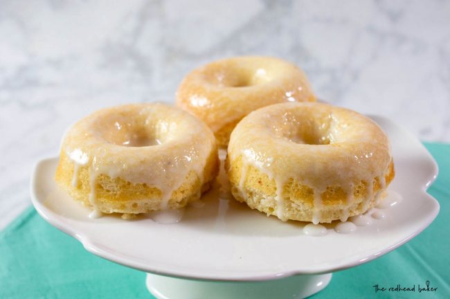 Three baked lemon donuts on a small white cake stand
