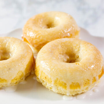 A close-up of three baked lemon donuts with coconut glaze