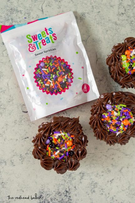 Three cauldron cakes around a bag of Sweets & Treats sprinkles