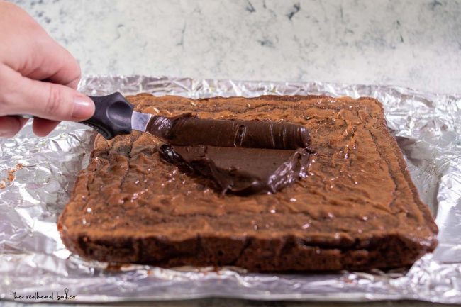 Chocolate icing being spread on a sheet of baked brownies