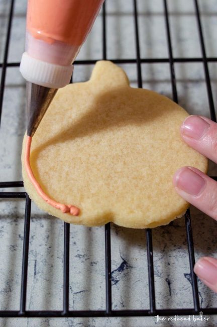 Piping orange icing onto a jack-o-lantern cookie