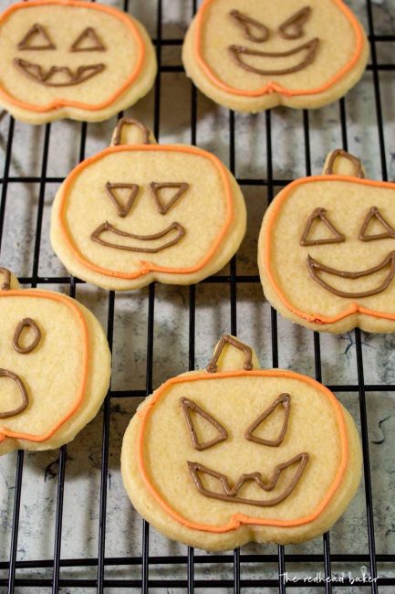 Six jack-o-lantern cookies with orange outlines and brown eyes and mouths